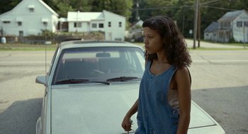 Movie still from “Bones and All” (2022), directed by Luca Guadagnino – A young woman standing next to a parked white car; Medium shot, Over the shoulder angle