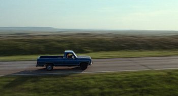 Movie still from “Bones and All” (2022), directed by Luca Guadagnino – A truck driving down a road near a grassy field; Extreme Wide shot, High angle