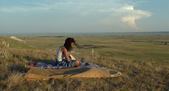 Movie still from “Bones and All” (2022), directed by Luca Guadagnino – A woman sitting on top of a blanket on top of a field; Wide shot, High angle