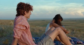 Movie still from “Bones and All” (2022), directed by Luca Guadagnino – Two people sitting on a blanket in a field; Medium shot, Over the shoulder angle