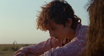 Movie still from “Bones and All” (2022), directed by Luca Guadagnino – A young man is looking down while sitting on the beach; Close Up shot, Over the shoulder angle
