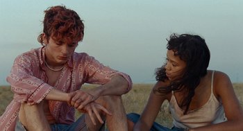 Movie still from “Bones and All” (2022), directed by Luca Guadagnino – A man and a woman sitting on the ground; Medium shot, Over the shoulder angle