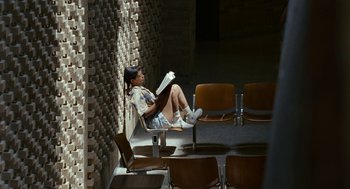 Movie still from “Bones and All” (2022), directed by Luca Guadagnino – A woman sitting on a chair reading a book; Wide shot, High angle