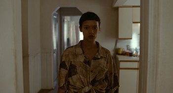 Movie still from “Bones and All” (2022), directed by Luca Guadagnino – A person standing in a room wearing a brown shirt; Medium shot, Over the shoulder angle