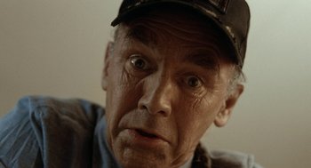 Movie still from “Bones and All” (2022), directed by Luca Guadagnino – An older man wearing a baseball cap stares into the camera; Extreme Close Up shot, Low angle