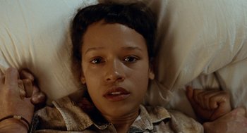 Movie still from “Bones and All” (2022), directed by Luca Guadagnino – A young woman laying in bed with a blanket; Close Up shot, Overhead angle