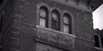 Movie still from “Fargo” (2014), created by Noah Hawley – An old brick building with a person looking out of a window; Wide shot, Low angle