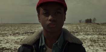 Movie still from “Fargo” (2014), created by Noah Hawley – A young man wearing a baseball cap in the middle of an open field; Close Up shot, Low angle
