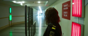 Movie still from “Border” (2018), directed by Ali Abbasi – A person with long brown hair is standing in a hallway; Medium shot, Over the shoulder angle