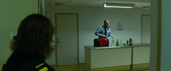 Movie still from “Border” (2018), directed by Ali Abbasi – A man in a uniform is standing at a counter with a bag; Wide shot, Low angle