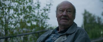 Movie still from “Border” (2018), directed by Ali Abbasi – An older man is looking at the camera while standing outside; Close Up shot, Over the shoulder angle