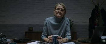 An older woman sitting at a table holding a coffee mug
