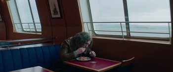 Movie still from “Border” (2018), directed by Ali Abbasi – A man sitting at a table eating a plate of food; Medium shot, High angle