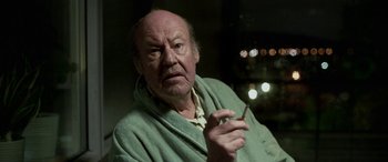 Movie still from “Border” (2018), directed by Ali Abbasi – An older man smoking a cigarette while wearing a robe; Close Up shot, Over the shoulder angle