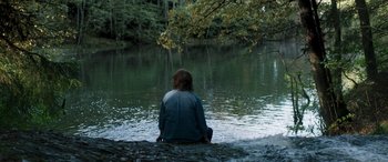 Movie still from “Border” (2018), directed by Ali Abbasi – A person sitting on a rock in a body of water; Extreme Wide shot, High angle