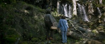 Movie still from “Border” (2018), directed by Ali Abbasi – A man and a woman standing in front of a waterfall; Wide shot, High angle