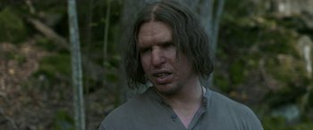 Movie still from “Border” (2018), directed by Ali Abbasi – A man with long black hair is standing in the woods; Close Up shot, Over the shoulder angle