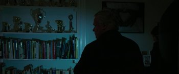 Movie still from “Border” (2018), directed by Ali Abbasi – A man standing in front of a book shelf at night; Medium shot, Over the shoulder angle