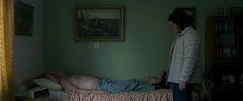 Movie still from “Border” (2018), directed by Ali Abbasi – A man laying on a bed next to a painting; Wide shot, Overhead angle