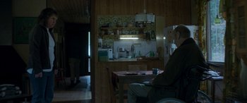 Movie still from “Border” (2018), directed by Ali Abbasi – A person sitting at a table in a kitchen; Wide shot, High angle