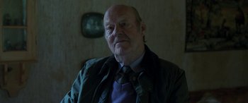 Movie still from “Border” (2018), directed by Ali Abbasi – An older man wearing a jacket and tie; Close Up shot, Over the shoulder angle
