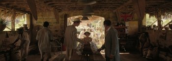 Movie still from “Breathe” (2017), directed by Andy Serkis – A group of people standing around a table with cups on top of it; Wide shot, Over the shoulder angle