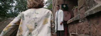 Movie still from “Breathe” (2017), directed by Andy Serkis – A man in a white lab coat standing next to a woman; Medium shot, Over the shoulder angle