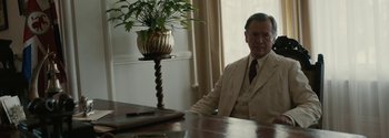 Movie still from “Breathe” (2017), directed by Andy Serkis – An older man sitting at a table with a plant; Medium shot, Over the shoulder angle