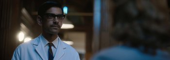 Movie still from “Breathe” (2017), directed by Andy Serkis – A man wearing a lab coat and glasses looks at the camera; Close Up shot, Over the shoulder angle