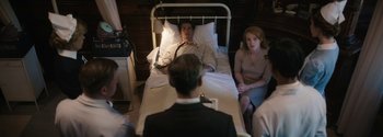 Movie still from “Breathe” (2017), directed by Andy Serkis – A man and a woman sitting in front of a man in a hospital bed; Medium shot, High angle