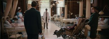 Movie still from “Breathe” (2017), directed by Andy Serkis – A man in a white lab coat stands in a hospital room; Wide shot, Over the shoulder angle