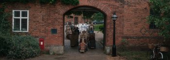Movie still from “Breathe” (2017), directed by Andy Serkis – A group of people walking down a brick path; Extreme Wide shot, High angle