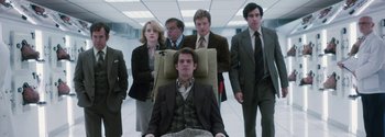 Movie still from “Breathe” (2017), directed by Andy Serkis – A group of people standing around a man sitting in a chair; Medium shot, Low angle