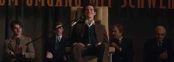 Movie still from “Breathe” (2017), directed by Andy Serkis – A man sitting in front of a microphone in front of two other men; Medium shot, Low angle