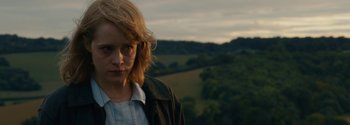 Movie still from “Breathe” (2017), directed by Andy Serkis – A woman with glasses is standing in front of a field; Close Up shot, Over the shoulder angle