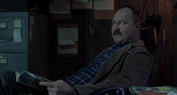 Movie still from “Brokeback Mountain” (2005), directed by Ang Lee – A man sitting in a chair holding a remote control; Close Up shot, Over the shoulder angle