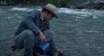 Movie still from “Brokeback Mountain” (2005), directed by Ang Lee – A man in a cowboy hat is pouring water into a blue cup; Medium shot, High angle