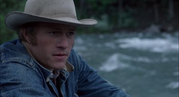 Movie still from “Brokeback Mountain” (2005), directed by Ang Lee – A man wearing a cowboy hat sitting in front of a body of water; Close Up shot, Over the shoulder angle