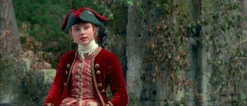 Movie still from “Brotherhood of the Wolf” (2001), directed by Christophe Gans – A woman in a red and white dress wearing a green hat; Medium shot, Over the shoulder angle