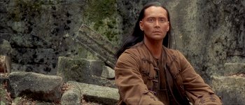 Movie still from “Brotherhood of the Wolf” (2001), directed by Christophe Gans – A man with long black hair sitting on rocks; Close Up shot, Over the shoulder angle