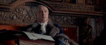 Movie still from “Brotherhood of the Wolf” (2001), directed by Christophe Gans – A person sitting in a chair wearing a coat; Medium shot, Low angle