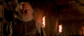 Movie still from “Brotherhood of the Wolf” (2001), directed by Christophe Gans – An old man with a beard and a white beard is sitting in front of a fire; Close Up shot, Low angle