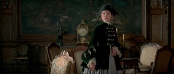 Movie still from “Brotherhood of the Wolf” (2001), directed by Christophe Gans – A woman in a green jacket standing next to a chair; Medium shot, Over the shoulder angle