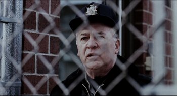 An older man wearing a hat looking through a chain link fence
