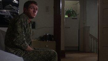 Movie still from “Bullitt” (1968), directed by Peter Yates – A man sitting on a chair in a living room; Medium shot, Over the shoulder angle