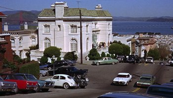 Movie still from “Bullitt” (1968), directed by Peter Yates – Cars are parked on the side of the road near a large building; Extreme Wide shot, High angle