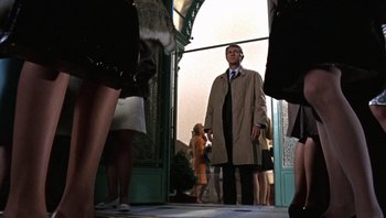 Movie still from “Bullitt” (1968), directed by Peter Yates – A man in a trench coat and tie standing in front of a doorway; Medium shot, Low angle