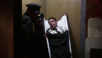 Movie still from “Bullitt” (1968), directed by Peter Yates – A police officer and two men standing next to a man in a blanket; Medium shot, High angle