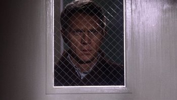 Movie still from “Bullitt” (1968), directed by Peter Yates – A man is looking through a window screen; Close Up shot, Low angle