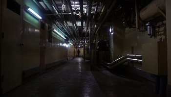 Movie still from “Bullitt” (1968), directed by Peter Yates – A dark hallway with pipes and a person walking in it; Extreme Wide shot, High angle